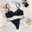 Ensemble lingerie noire en dentelle composé d’un soutien-gorge et d’un string posé sur une surface claire avec accessoires féminins.